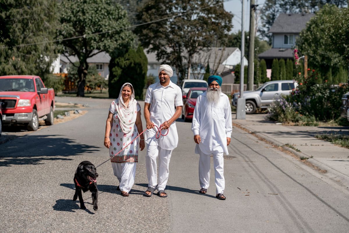 Indian family walking their black dog down a quiet street