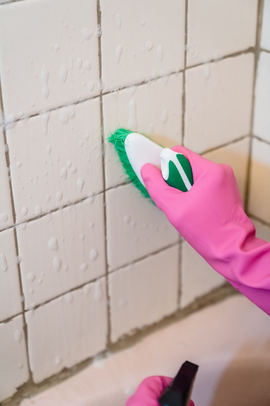 Gloved hand scrubbing tiles with a brush